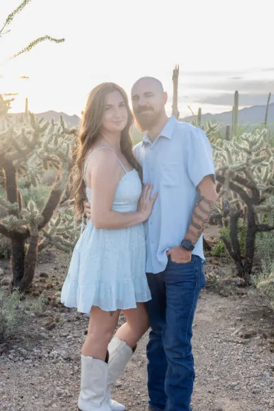 Couple posing together at golden hour in a desert landscape with saguaro cacti and mountains in the background.