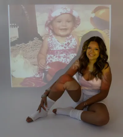 Smiling woman sitting before projected baby photo in nostalgic birthday portrait session.