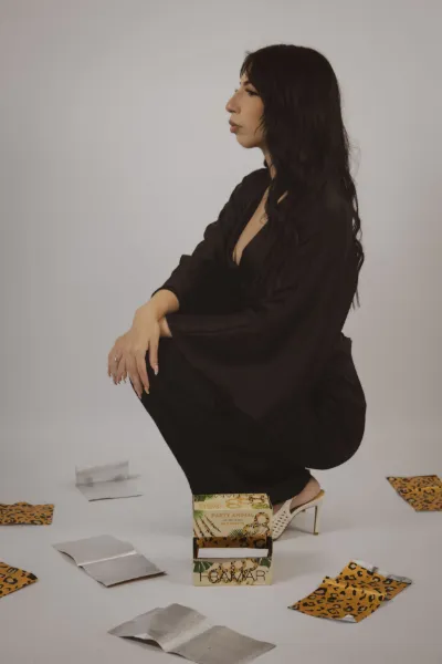 Woman in black outfit crouching beside decorative box with scattered papers on studio floor.