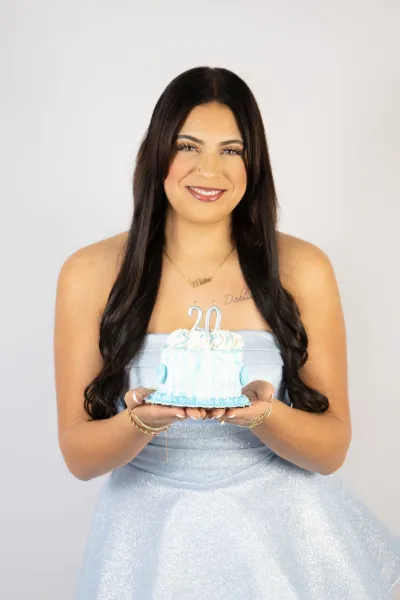 Smiling woman in blue strapless dress holding 30th birthday cake on white background.