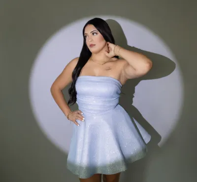 Plus-size woman posing in strapless sparkly light blue mini dress under a spotlight against green background.