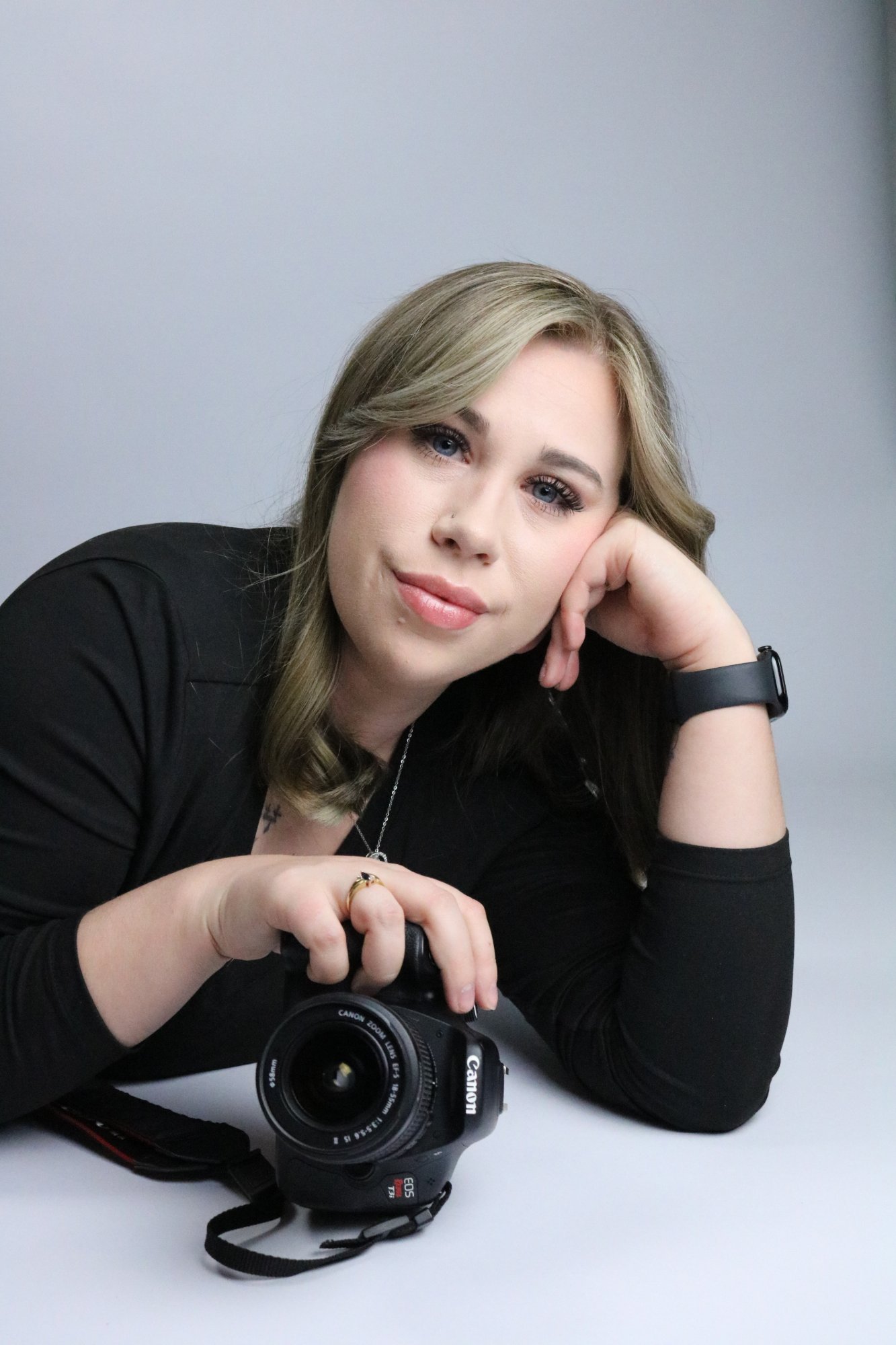 Alicia, owner of Alicia & Co. Photography LLC, posing with her Canon camera against a grey studio background.