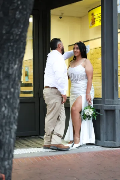 Groom in white shirt tenderly touches bride's face as she holds white bouquet in doorway.