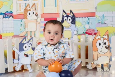 Smiling baby boy sitting in front of a colorful Bluey cartoon themed backdrop with toys.
